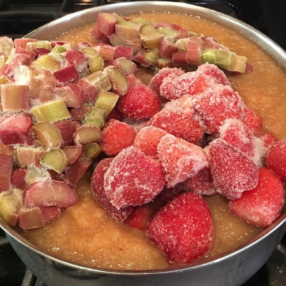 Pot on stove filled with applesauce, frozen strawberries and rhubarb.